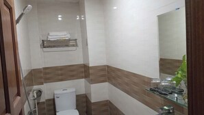 Egy fürdőszoba, amelyben található egy WC, egy üvegpolc, rajta a tisztálkodási eszközökkel, és egy tükör.