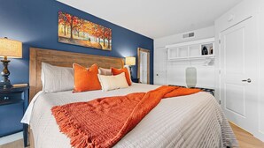 A bedroom with a large bed, a headboard, a painting on the wall, a bedside table with a lamp, and a wardrobe.