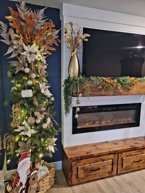 Un árbol de Navidad decorado con adornos y luces, una chimenea con repisa, y un televisor encima.