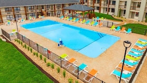 A hotel with a large outdoor pool, multiple lounge chairs, and a covered seating area.