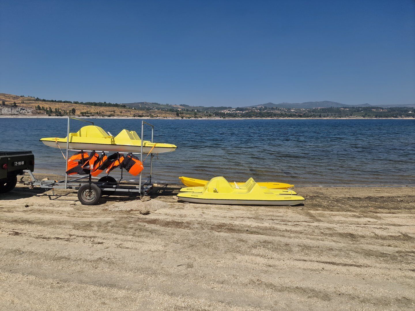 A beach with two yellow boats and a cart with life jackets.
