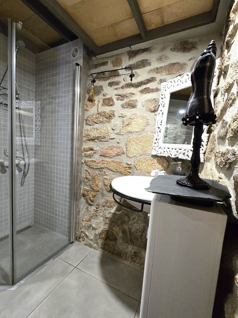A bathroom with a shower, a sink, a mirror, and a stone wall.