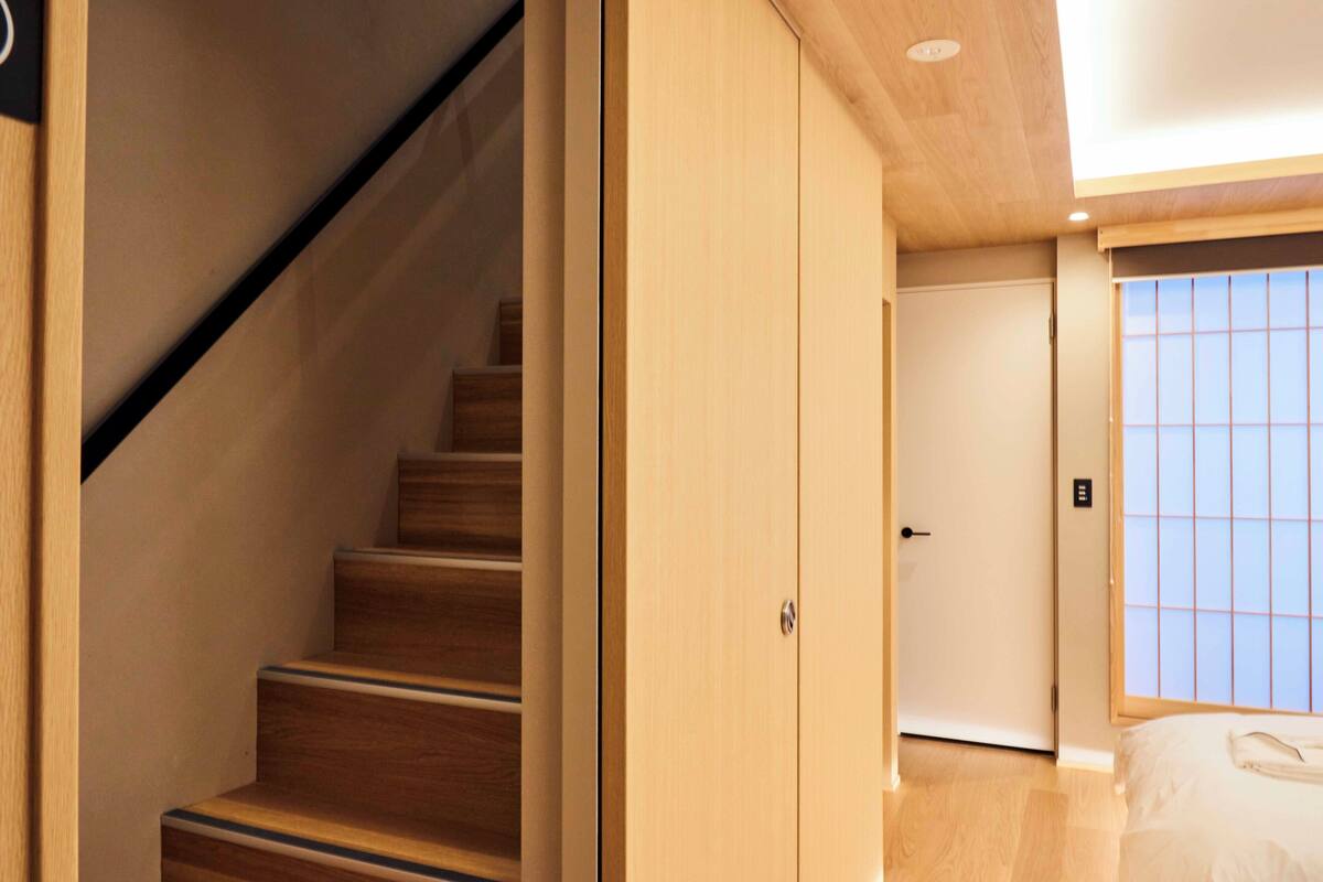 Una scala conduce a una stanza con una porta scorrevole e vista su una finestra con un motivo a griglia.