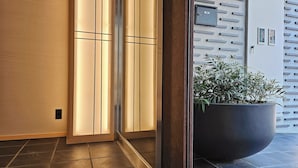 Un interior moderno con suelo de madera, una planta grande en maceta y una caja fuerte anclada a la pared.