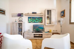 A living room with a TV, white chairs, a cabinet, and artwork on the walls.