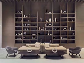 Un salon moderne comprenant un ensemble canapé et deux fauteuils, une table basse et une grande étagère remplie d’objets décoratifs.