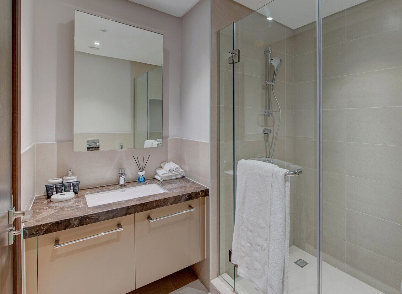 Une salle de bain moderne avec une douche à parois de verre, un grand miroir et un comptoir en marbre.