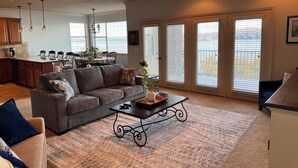 A spacious living room with a gray sofa, a coffee table, and a dining area in the background.