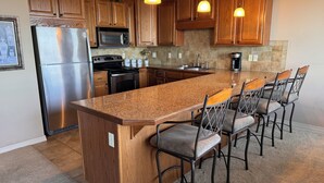A kitchen with wooden cabinets, stainless steel appliances, a granite countertop, and bar stools.