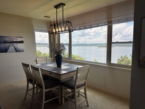A dining area with a view of a lake, a table with chairs, a vase with flowers, and a painting on the wall. - Panoramic Lake View!! - The View at Emerald Pointe (Hollister)
