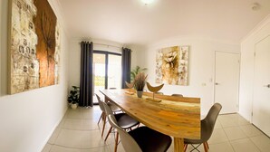 A dining area with a wooden table, six chairs, and a large abstract painting on the wall.
