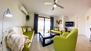 A modern living room with a green sofa, a glass coffee table, and a ceiling fan.