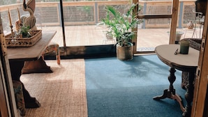 Amplia habitación con un amplio ventanal corredera que da a una terraza exterior. La habitación cuenta con una alfombra azul, un tapete de bienvenida y una mesa de madera con un centro de mesa decorativo con forma de cisne.