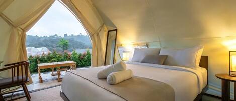 A tent-style bedroom with a bed, bedside tables, and a view of greenery outside.