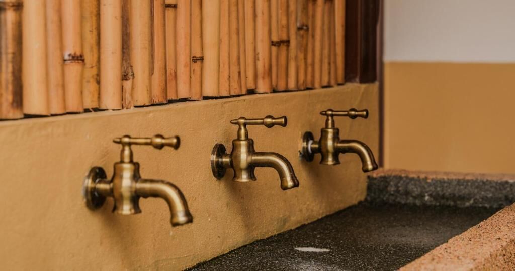 Three brass faucets mounted on a wall with a bamboo backdrop.