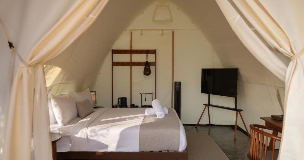 A cozy, well-lit tented room with a bed, a TV, and a small table.