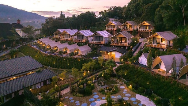 Un resort con varias cabañas, un jardín central y montañas al fondo.