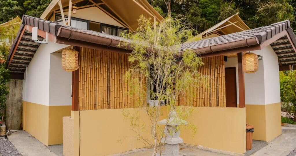 En traditionell japansk byggnad med ett tak täckt av tegelpannor, träväggar och en liten trädgård med ett träd och en stenlykta.