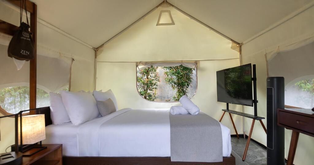 Habitación con tienda de campaña, cama, televisor y ventana con vistas a zonas verdes.