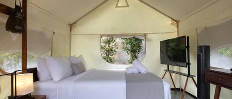Habitación con tienda de campaña, cama, televisor y ventana con vistas a zonas verdes.
