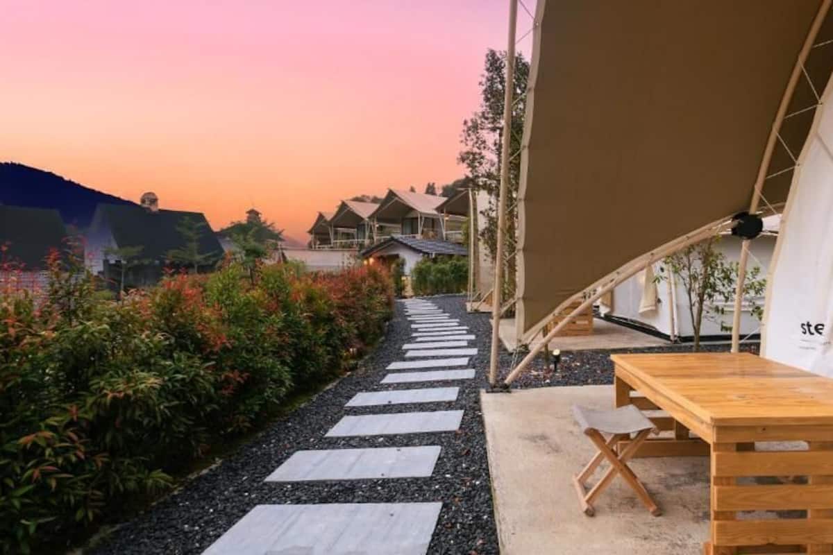 A pathway leading to a wooden bench and a tented area with a view of houses and a sunset.