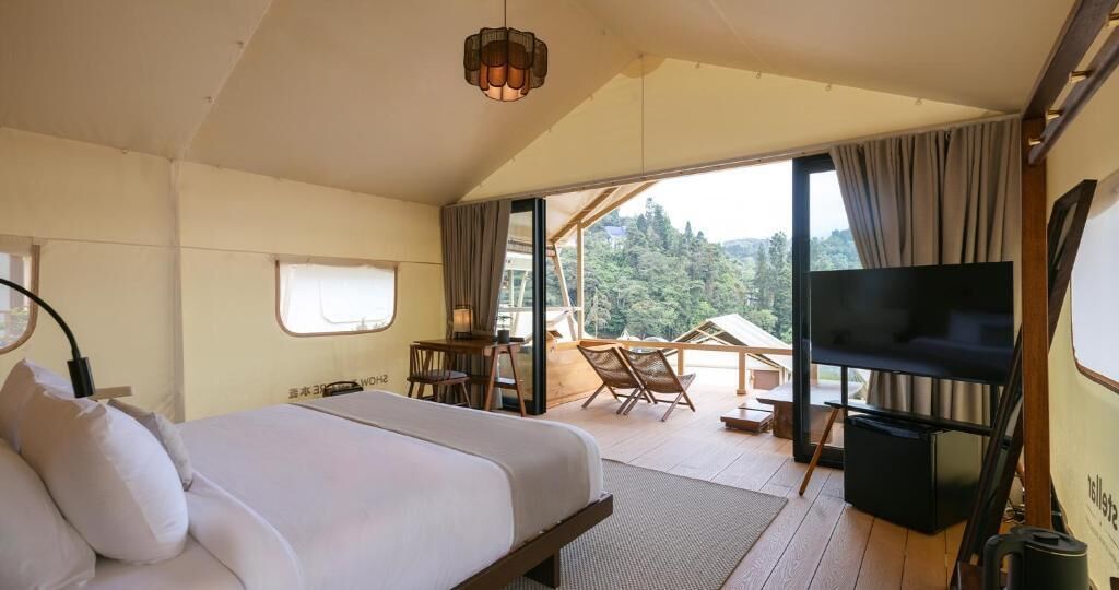 Quarto com cama, televisão, escrivaninha e varanda com cadeiras.