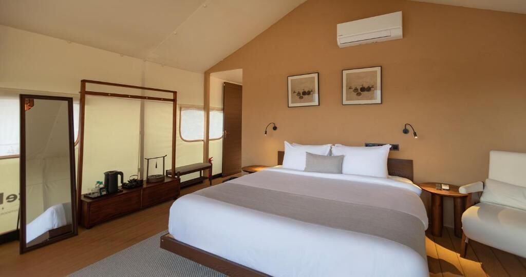 A hotel room with a large bed, a desk, a chair, and a wardrobe.