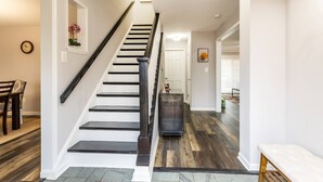 Un escalier avec une rampe sombre et des marches blanches, menant à une pièce dotée d’un plancher en bois et d’une porte blanche.