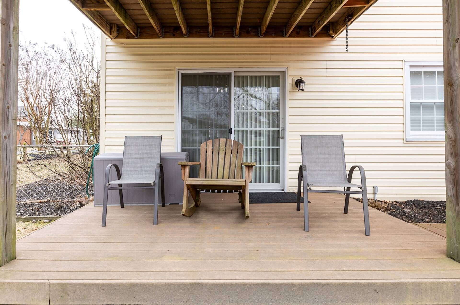 Une véranda avec deux chaises et une table, une chaise en bois et une porte-fenêtre coulissante.