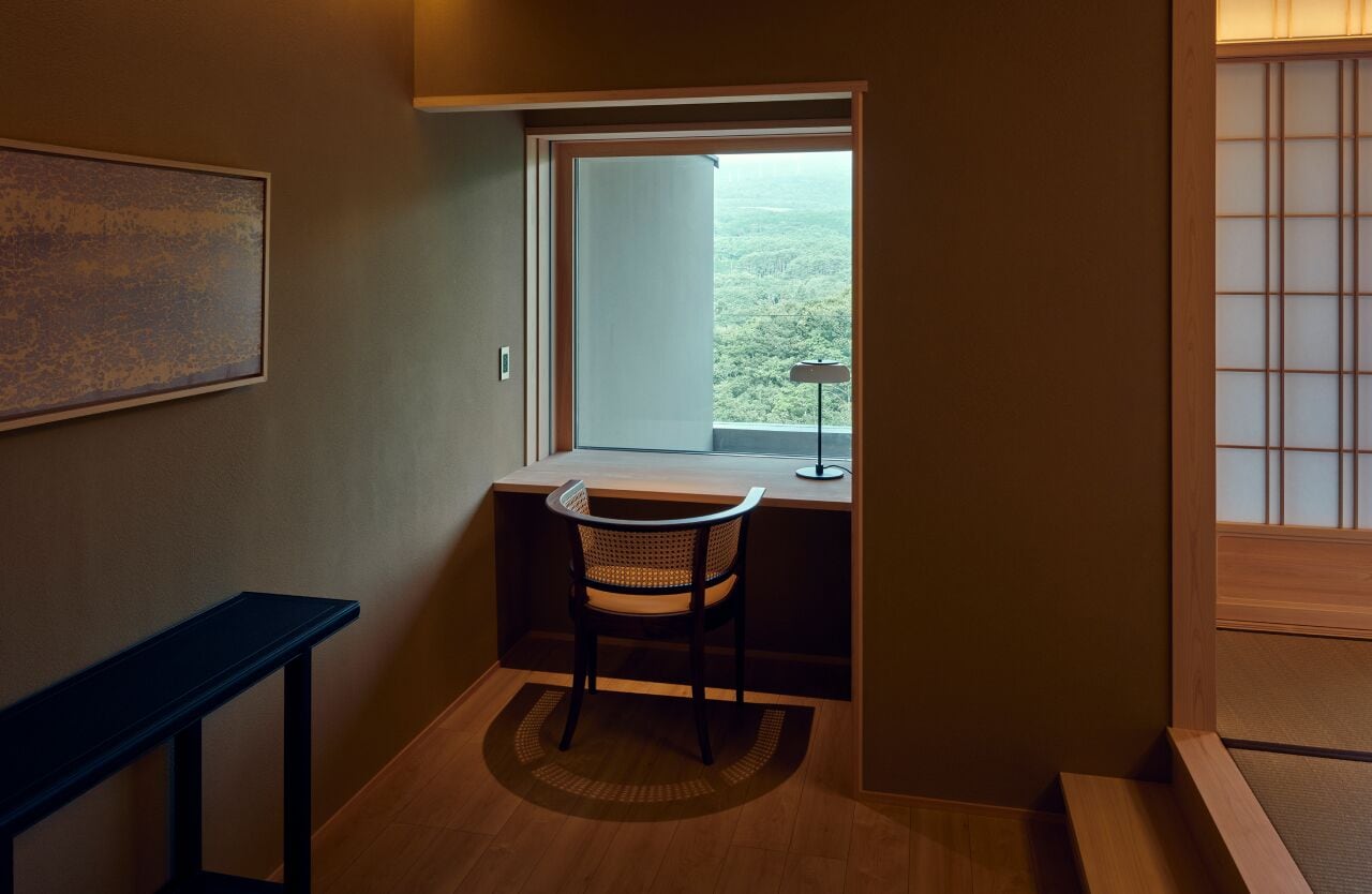 A small, private office with a desk, chair, and a large window offering a view of a forested landscape.