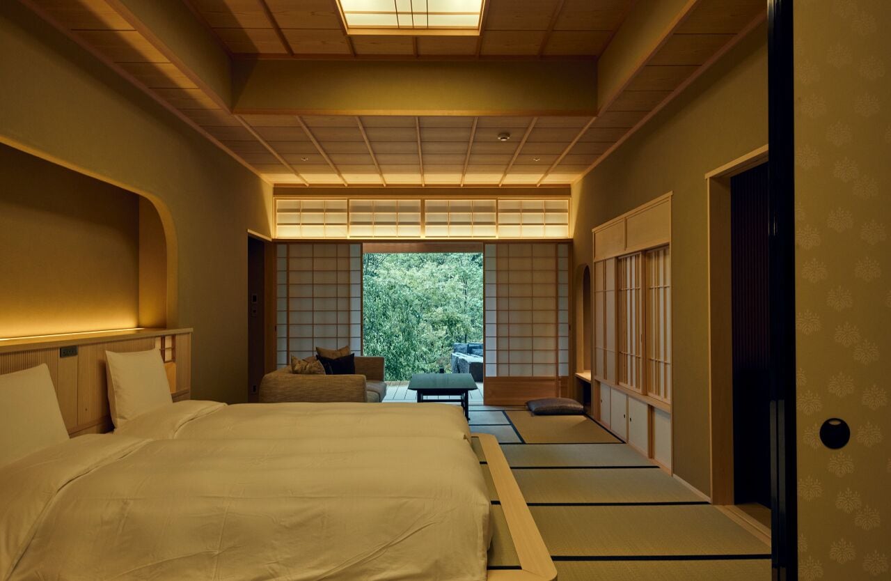 A traditional Japanese-style bedroom with tatami flooring, a large bed, sliding doors, and a view of greenery outside.