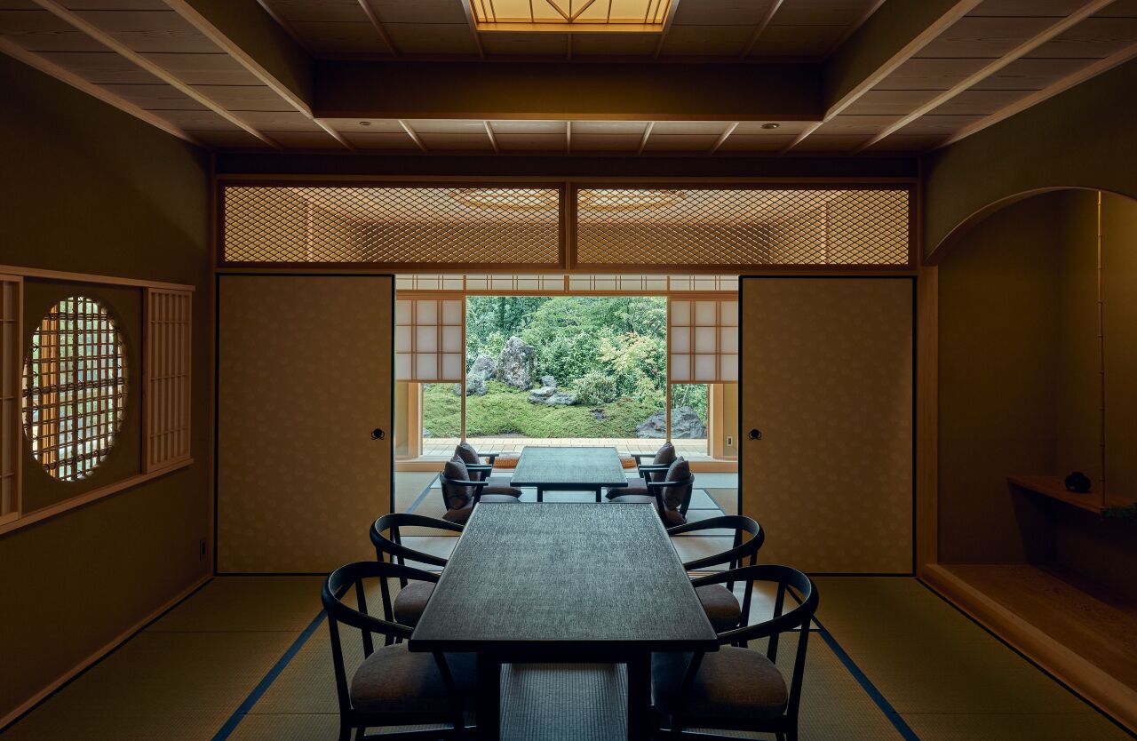 A traditional Japanese room with tatami flooring, a low table with cushions, and a view of a garden through shoji screens.