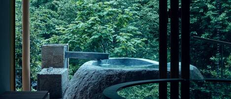 A serene outdoor area with a stone water feature and seating, surrounded by lush greenery.
