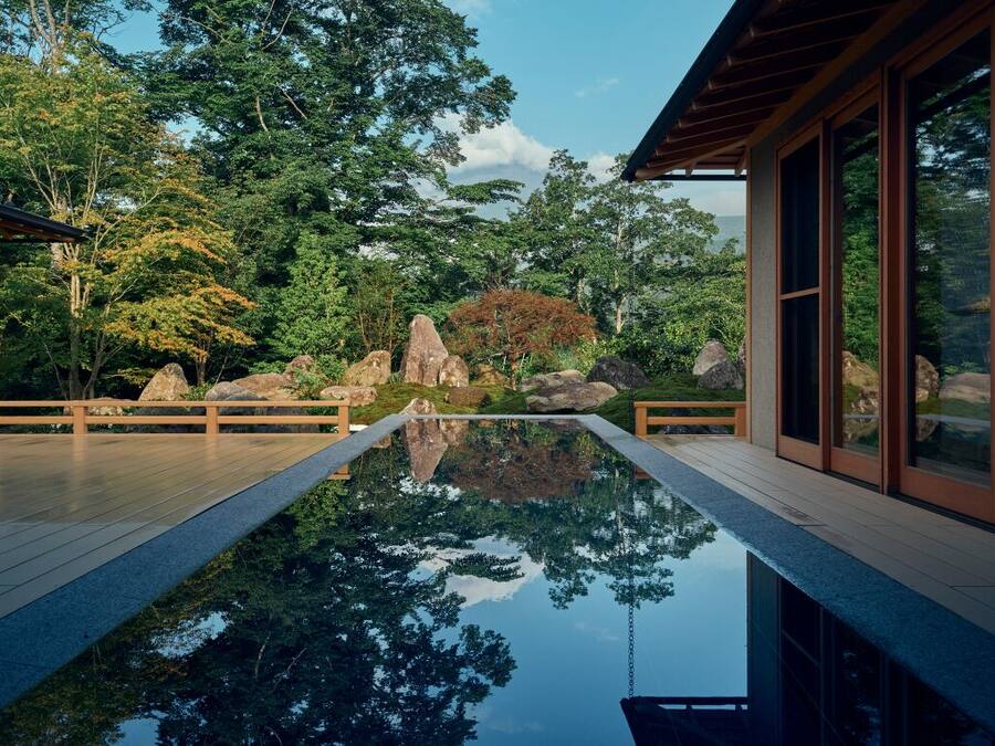 A serene pool area with a wooden deck, surrounded by large rocks and lush greenery.