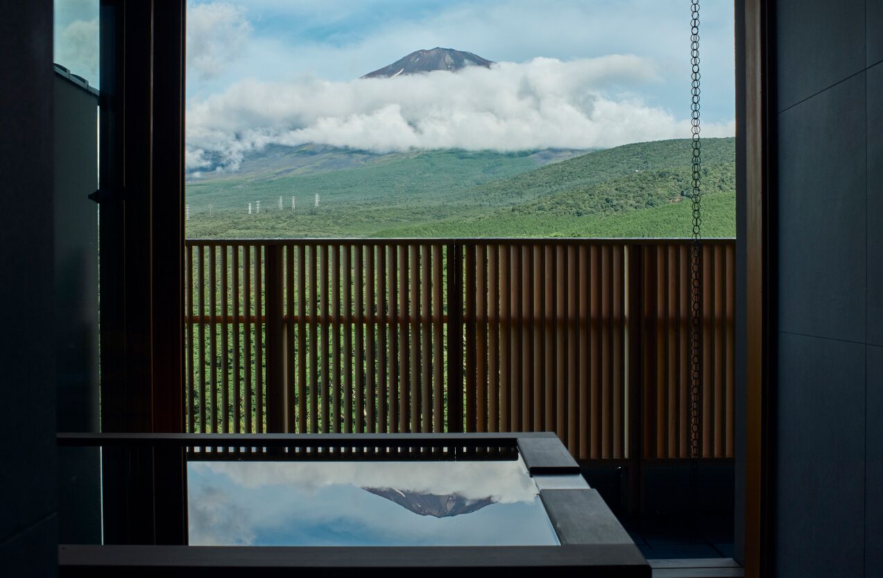 Ein Zimmer mit Blick auf einen Berg und Wolken, durch eine Holzlamellenabtrennung hindurch.
