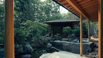 A traditional Japanese garden with a wooden pavilion, rock formations, and a small water feature.