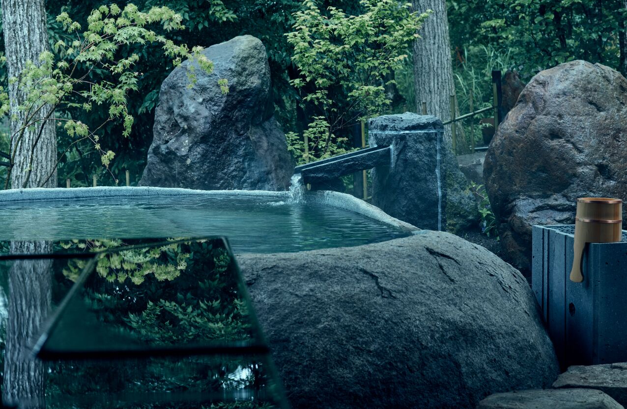 A tranquil outdoor setting with a small pond, large rocks, and a wooden structure.