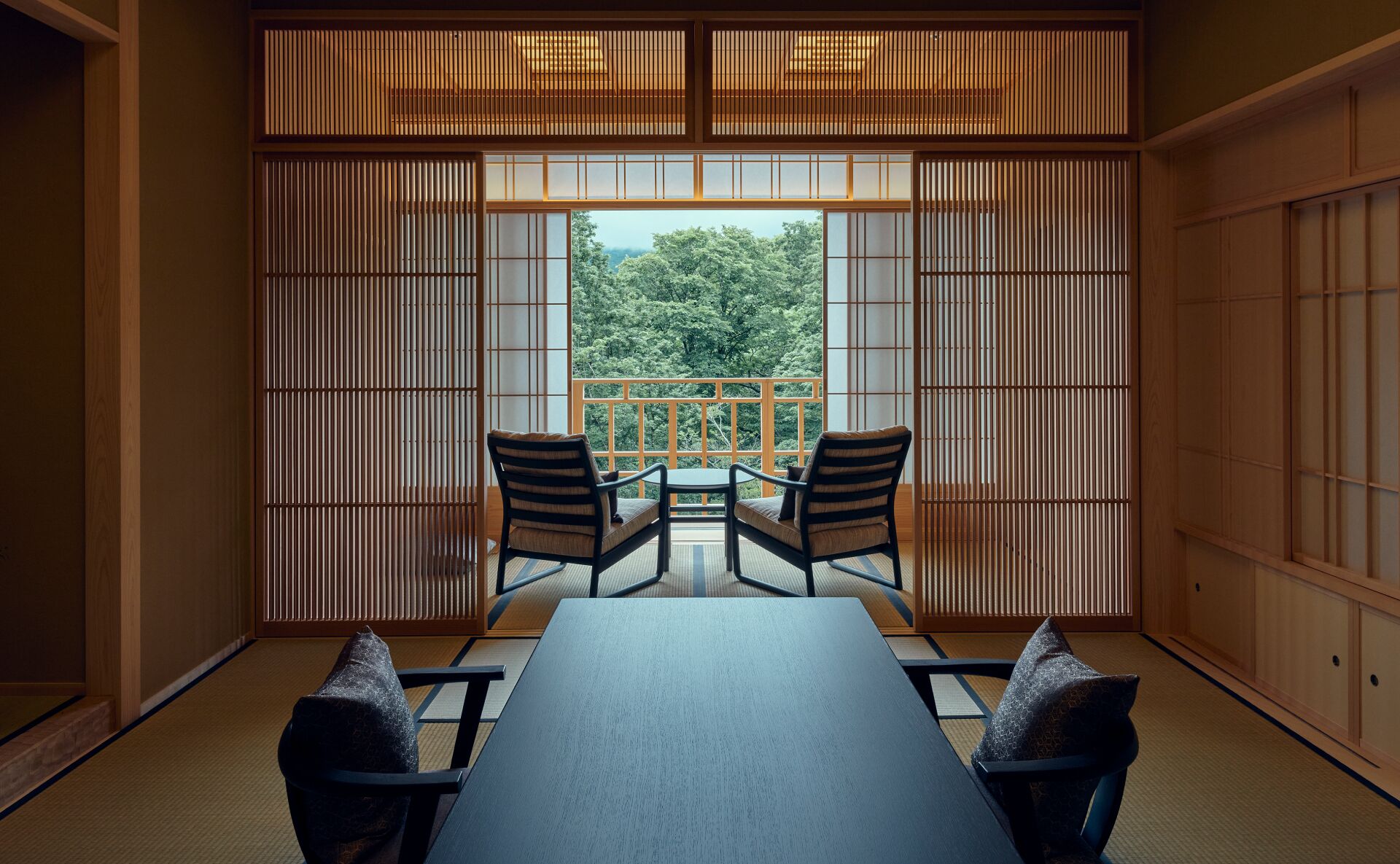 A traditional Japanese room with tatami flooring, a low table, two chairs, and shoji screens.