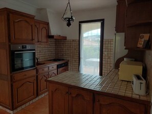 A kitchen with wooden cabinets, a built-in oven, a dishwasher, a tiled backsplash, a hanging light fixture, and a window with a view.