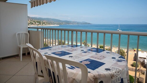 A balcony with a table and chairs, overlooking a beach with a sailboat and a distant shoreline. - Beautiful T2 for 4 people for rent in Le Lavandou, facing the sea. (LE LAVANDOU)