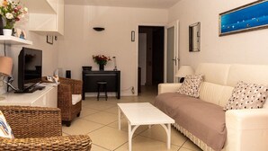 A compact living space with a sofa, a small table, a TV, a desk with a computer, and a chair. - Beautiful T2 for 4 people for rent in Le Lavandou, facing the sea. (LE LAVANDOU)