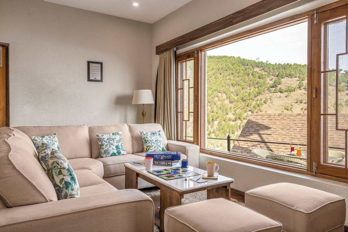 A living room with a beige sofa, a coffee table, and a view of a hilly landscape through large windows.