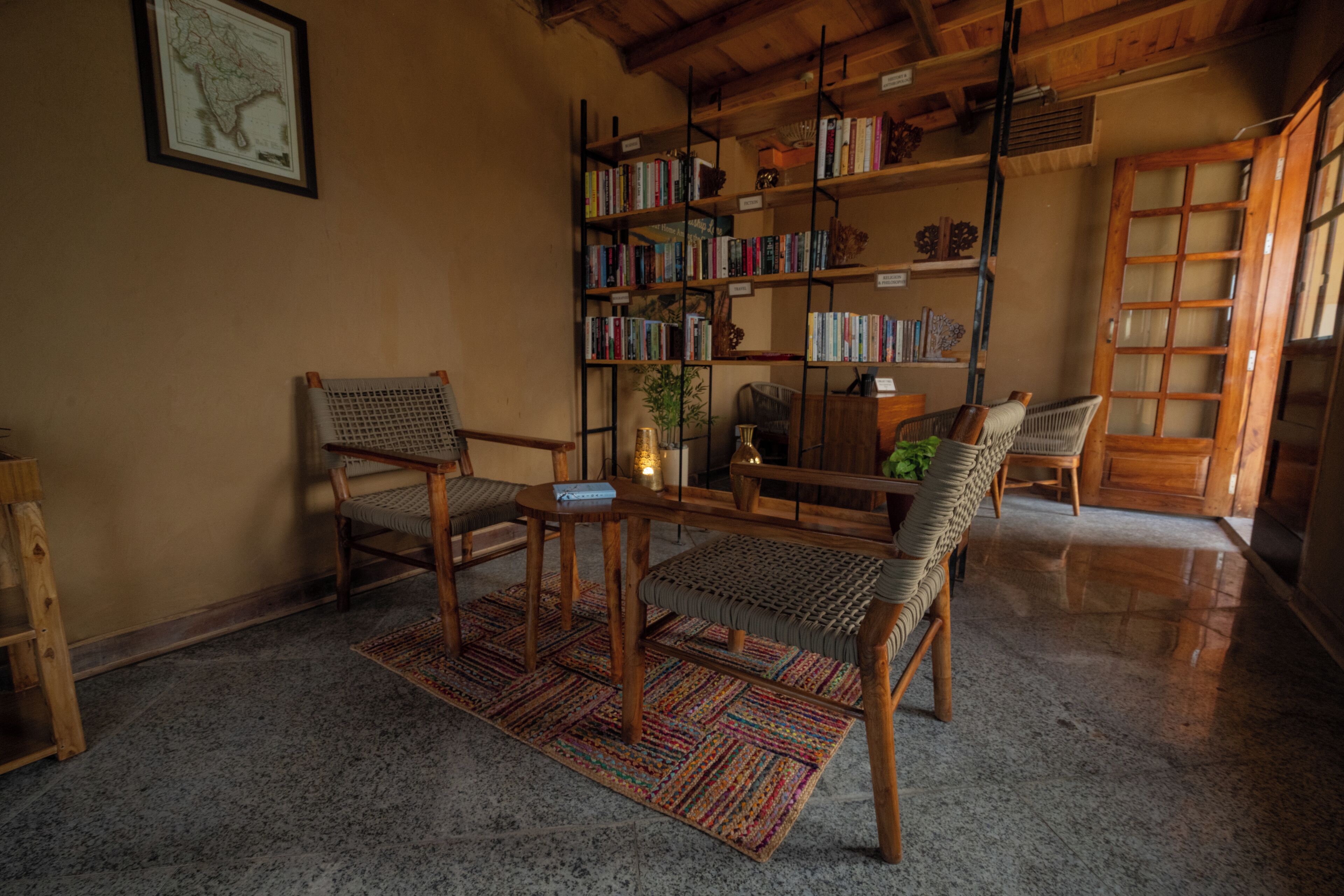 A cozy living room with a wooden bookshelf, two wicker chairs, a coffee table, and a patterned rug.