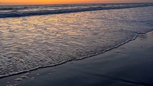 Una playa al atardecer con olas lamiendo suavemente la orilla.
