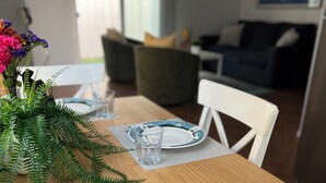 Una mesa de comedor servida con platos, vasos y cubiertos, un florero con flores y una planta verde.