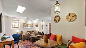 A living room with a sofa, armchair, coffee table, and a small dining table with a plant.