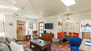 A living room with a wooden coffee table, a blue armchair, and a sofa. There is a television on the wall and a wooden cabinet.