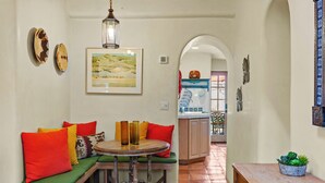 A cozy living area with a round table, green cushioned seating, and a framed landscape painting.