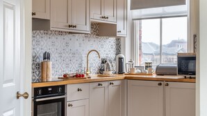 Une cuisine avec des meubles blancs, un four encastré, une machine à café et un four à micro-ondes.