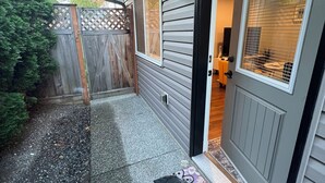 Ein Wohnhausfassade mit grauer Tür, Fußmatte und kleinem Garten.